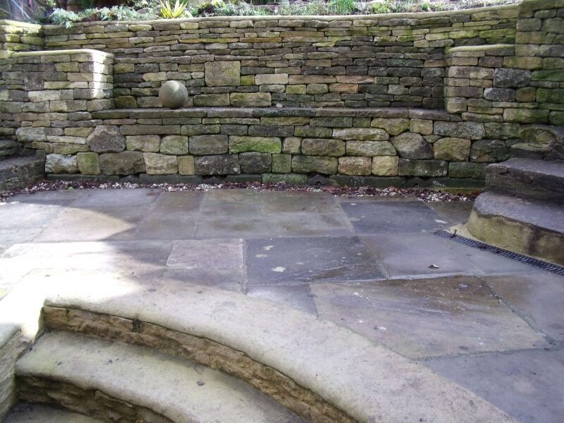 Curved dry stone garden bench built into retaining wall with stone spheres, Bladon