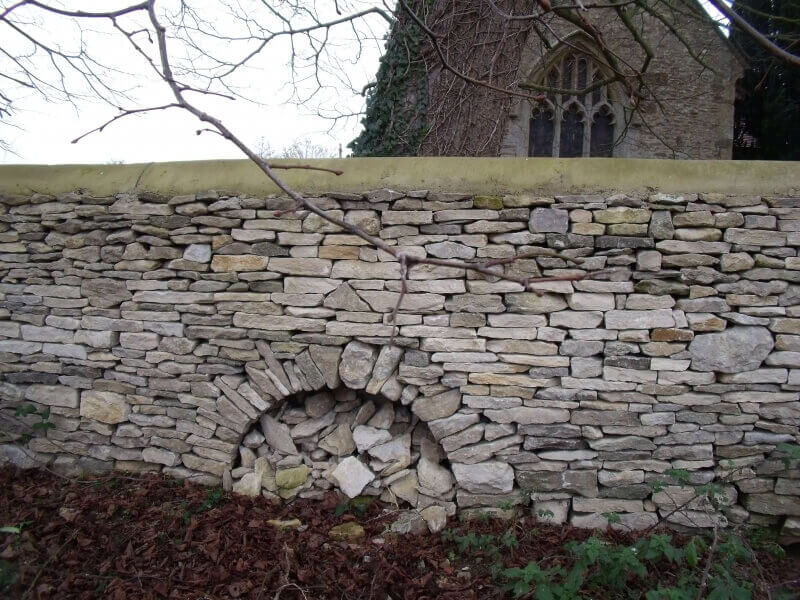 Decorative radial stone arch built into churchyard dry stone wall around tree roots