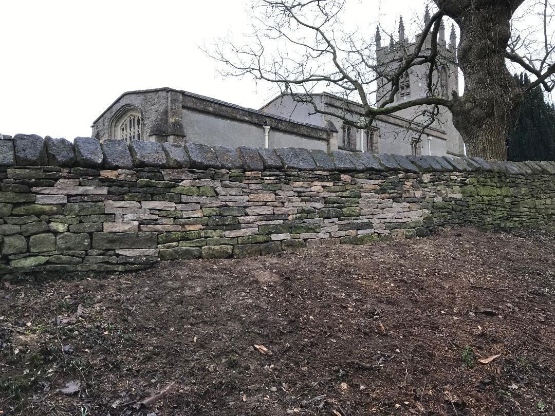 Restored churchyard dry stone wall at Great Rollright with church tower behind