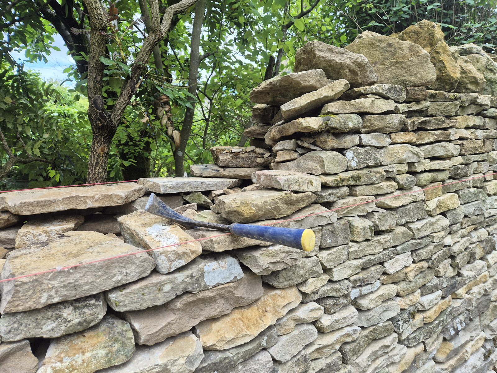 Walling hammer and stones on top of dry stone wall under construction
