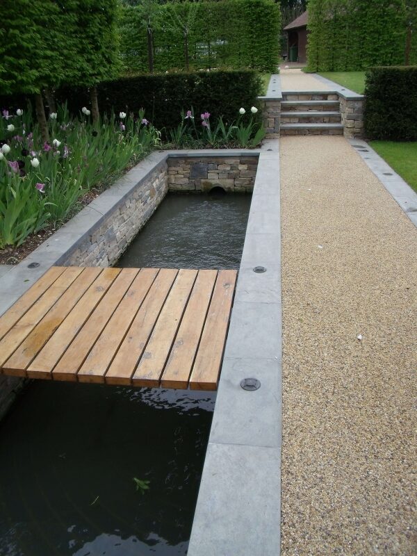 Dry stone walls framing a water rill with timber bridge in a formal garden