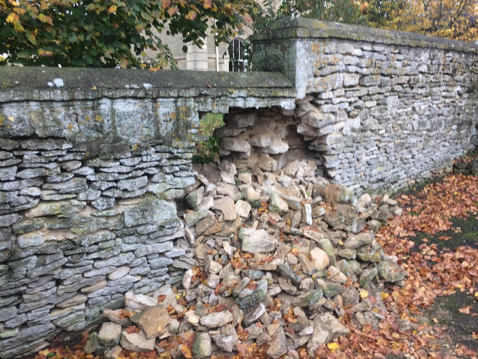 Large collapsed section of coped estate dry stone wall with fallen stone pile in autumn leaves